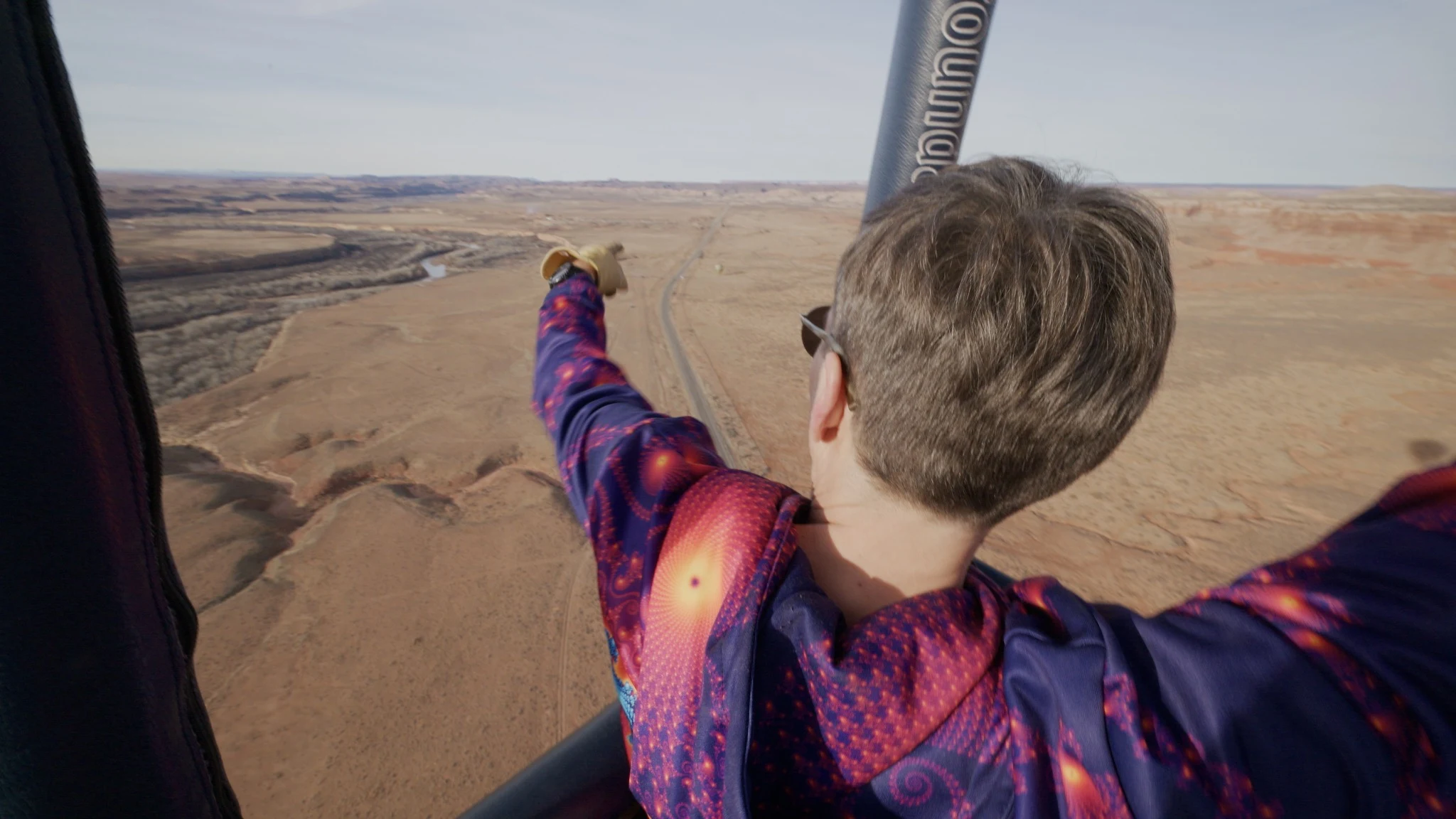 A passenger points out across the landscape from a balloon basket.