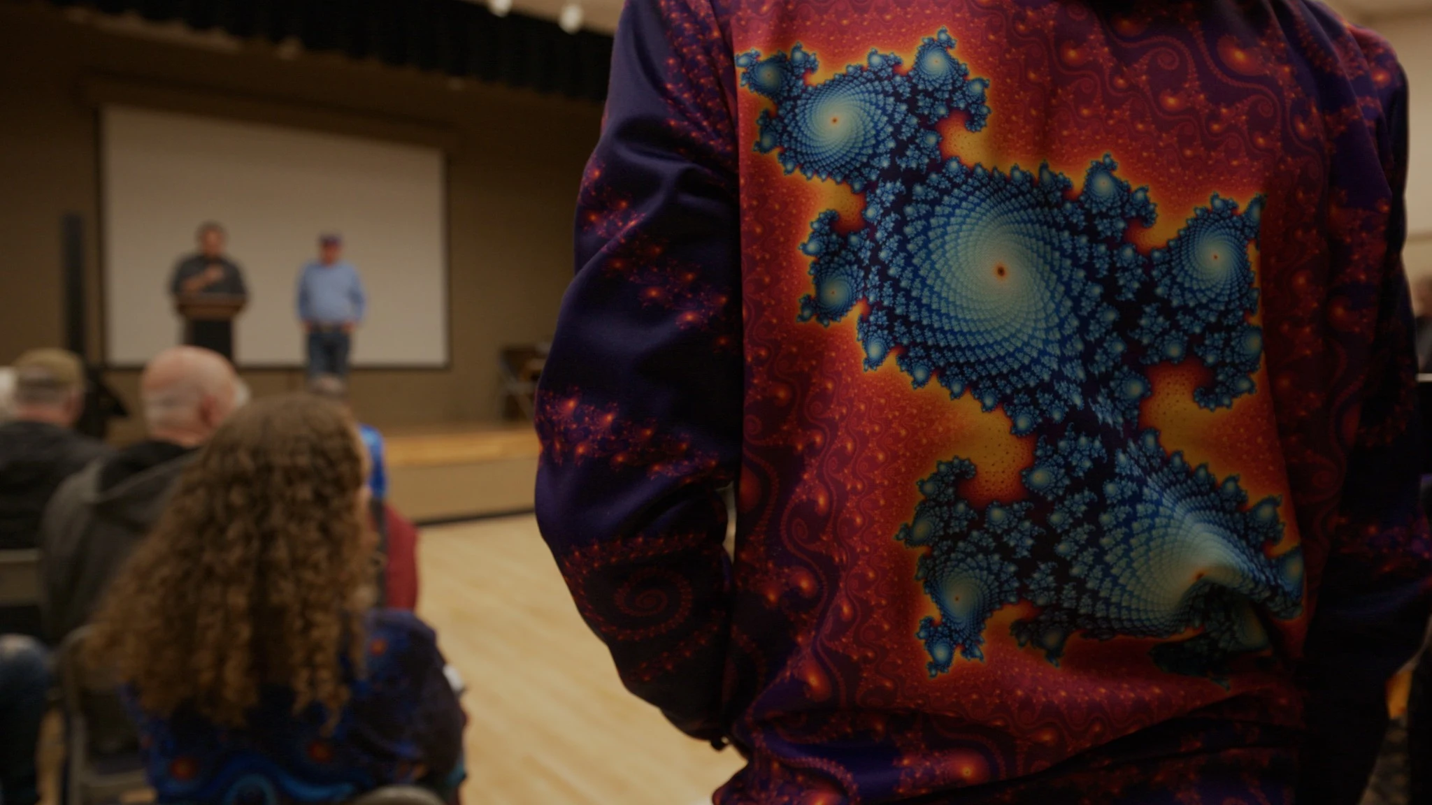 A bright fractal pattern across the back of a shirt at a community gathering.
