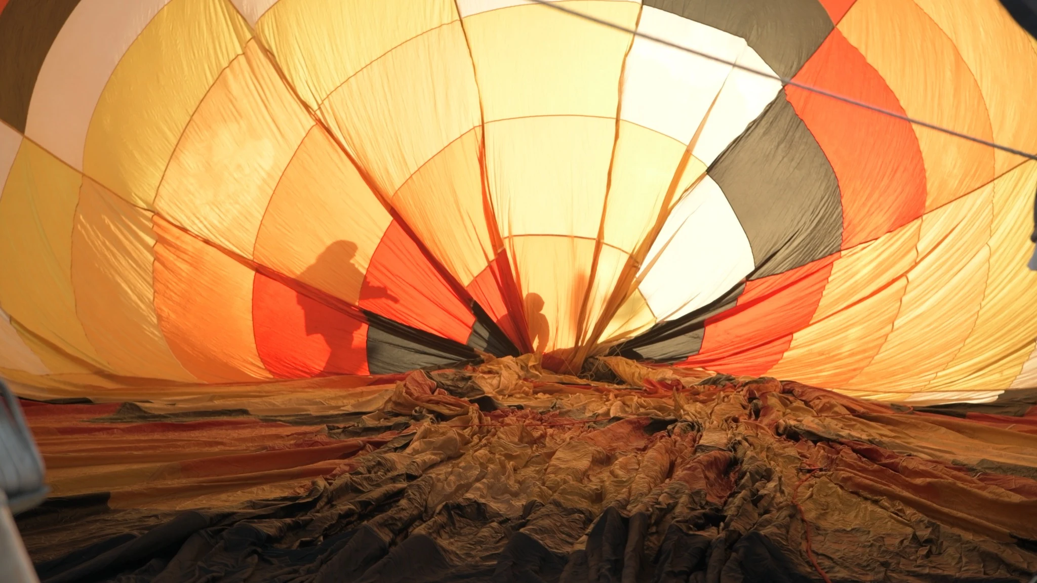 Silhouetted people working inside a sunlit balloon envelope.