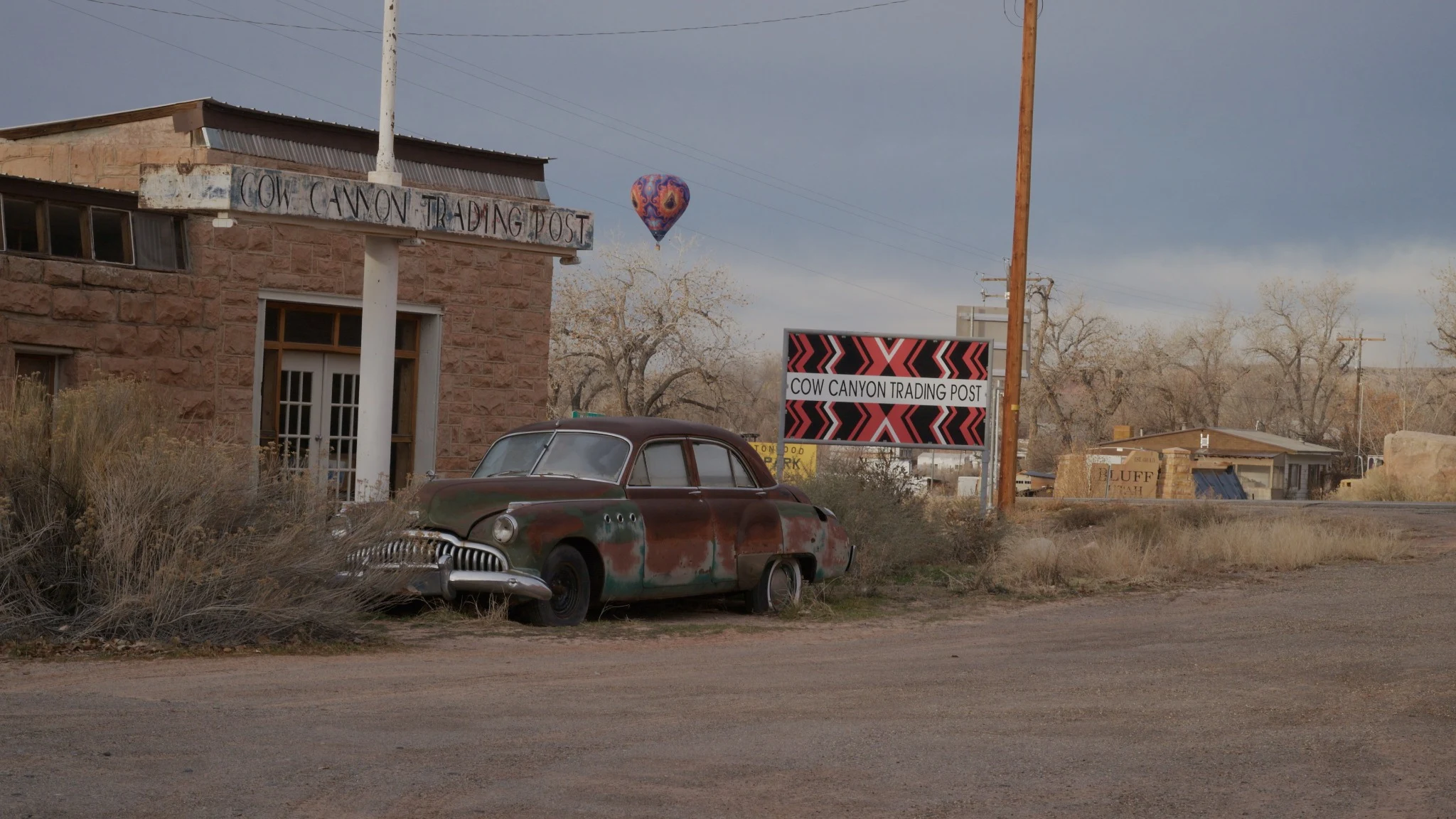 A rusty Buick outside Cow Canyon Trading Post, with a balloon in the distance.