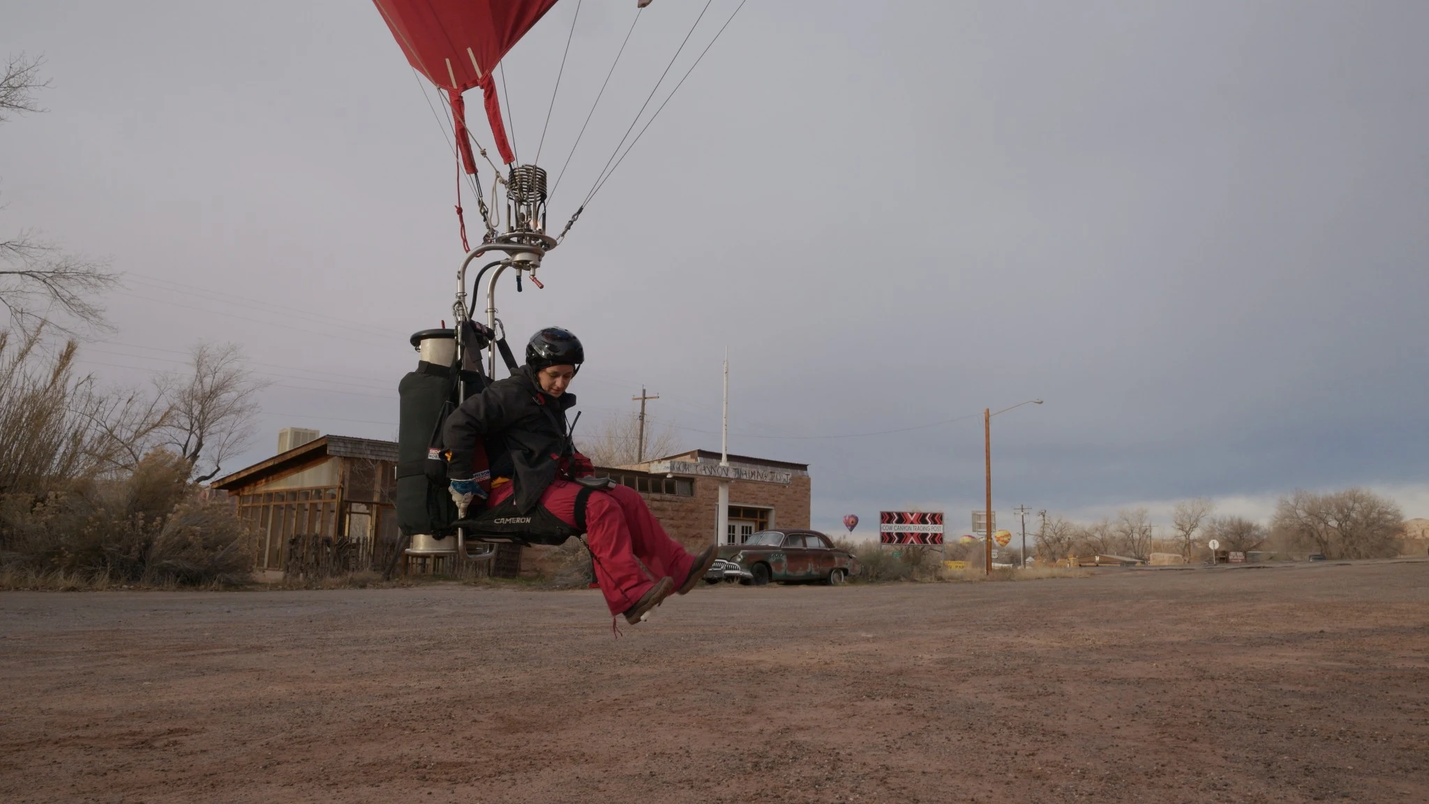 A passenger suspended beneath a red balloon, just above the ground.