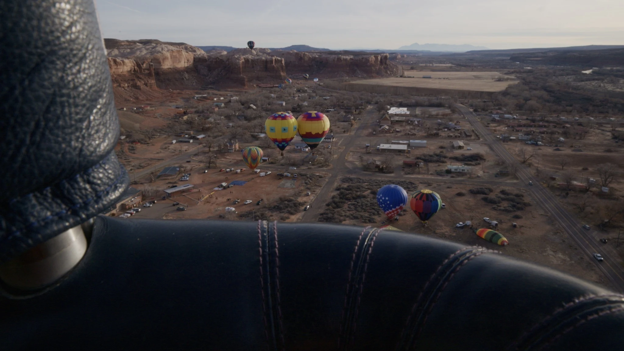 The view past the edge of a balloon basket toward distant balloons and open country.