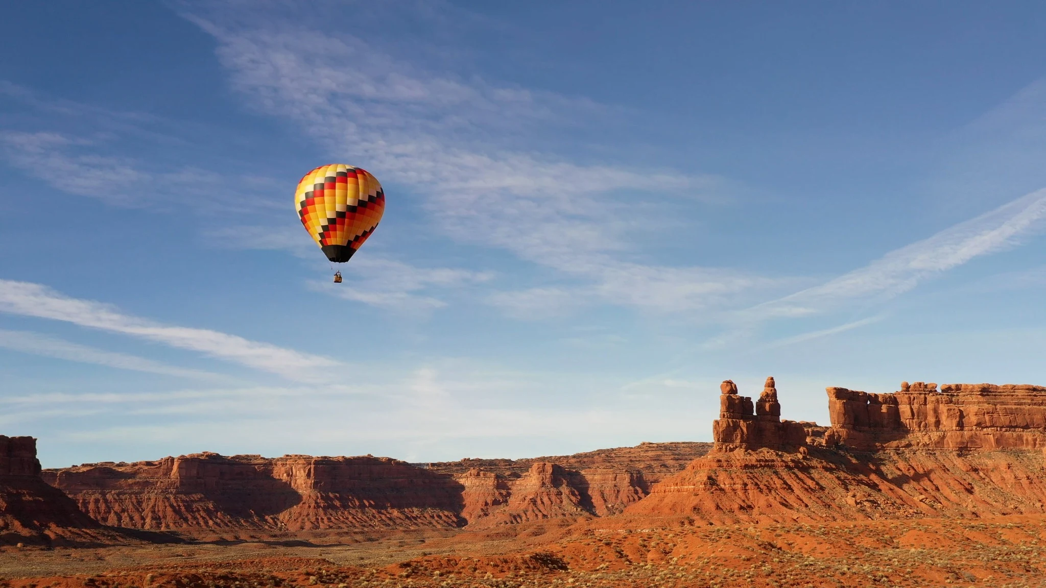 A striped balloon above red cliffs beneath a broad blue sky.