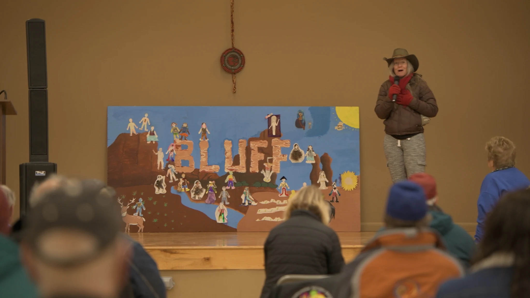 A speaker and a handmade Bluff mural at a community gathering.