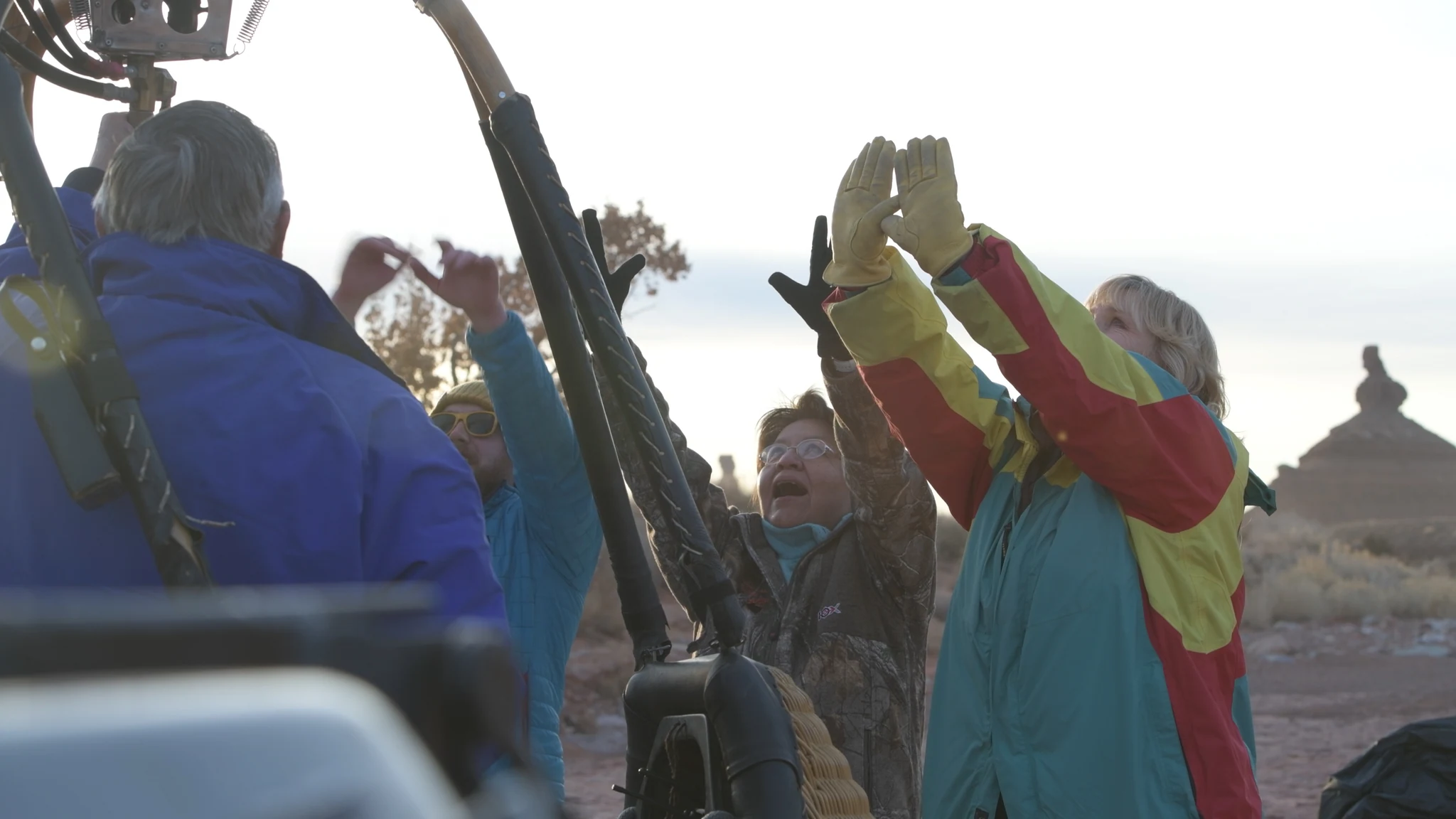 People raising their gloved hands beside a balloon in the winter light.