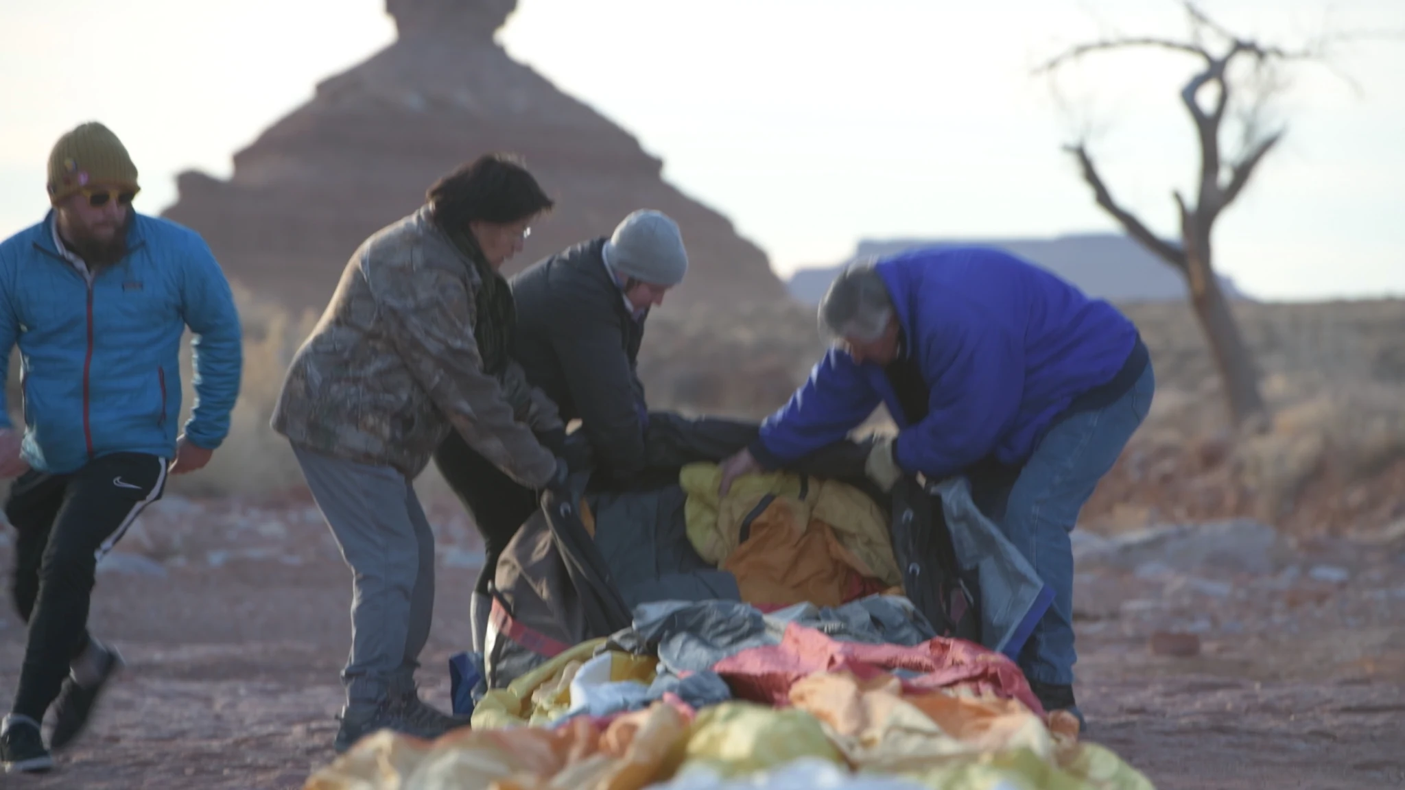 People gathering a balloon envelope together beneath red rock formations.