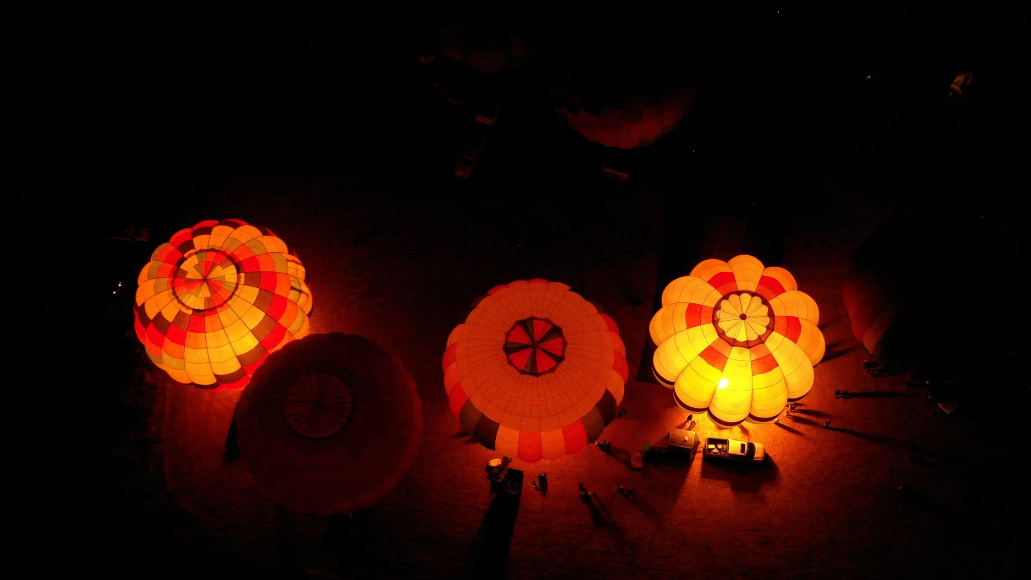 Looking down on illuminated balloon envelopes and the people gathered below.