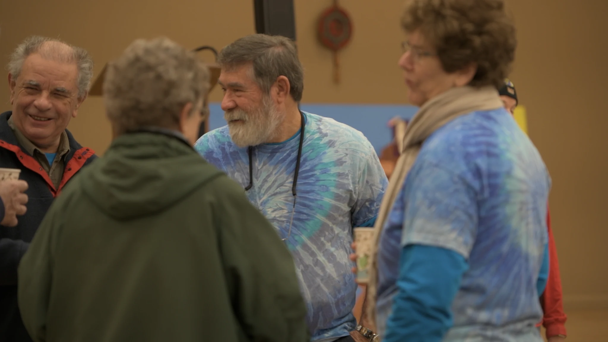 Friends in tie-dyed shirts talking over coffee at a gathering.