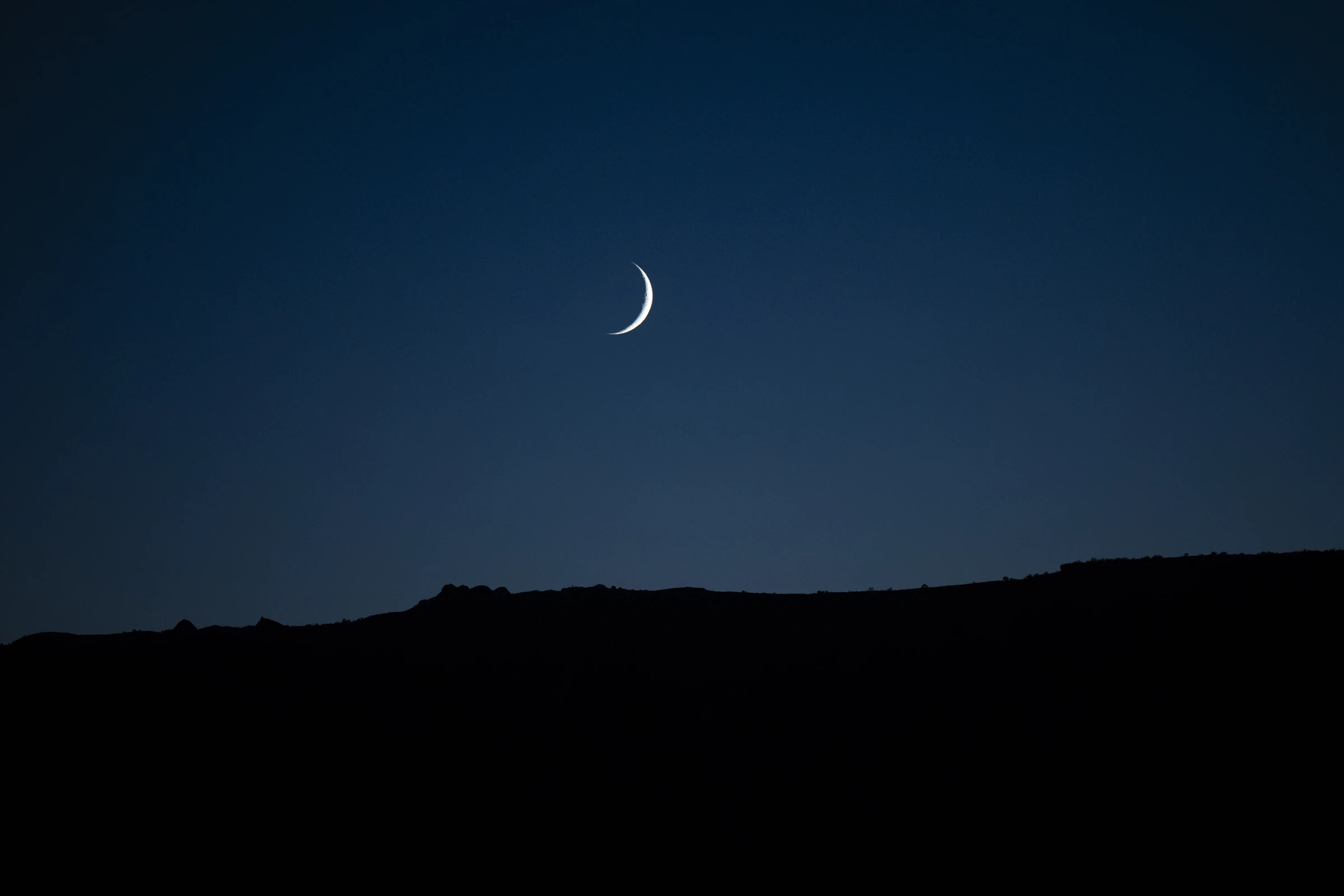 A crescent moon above the silhouetted landscape of Canyonlands National Park, Utah