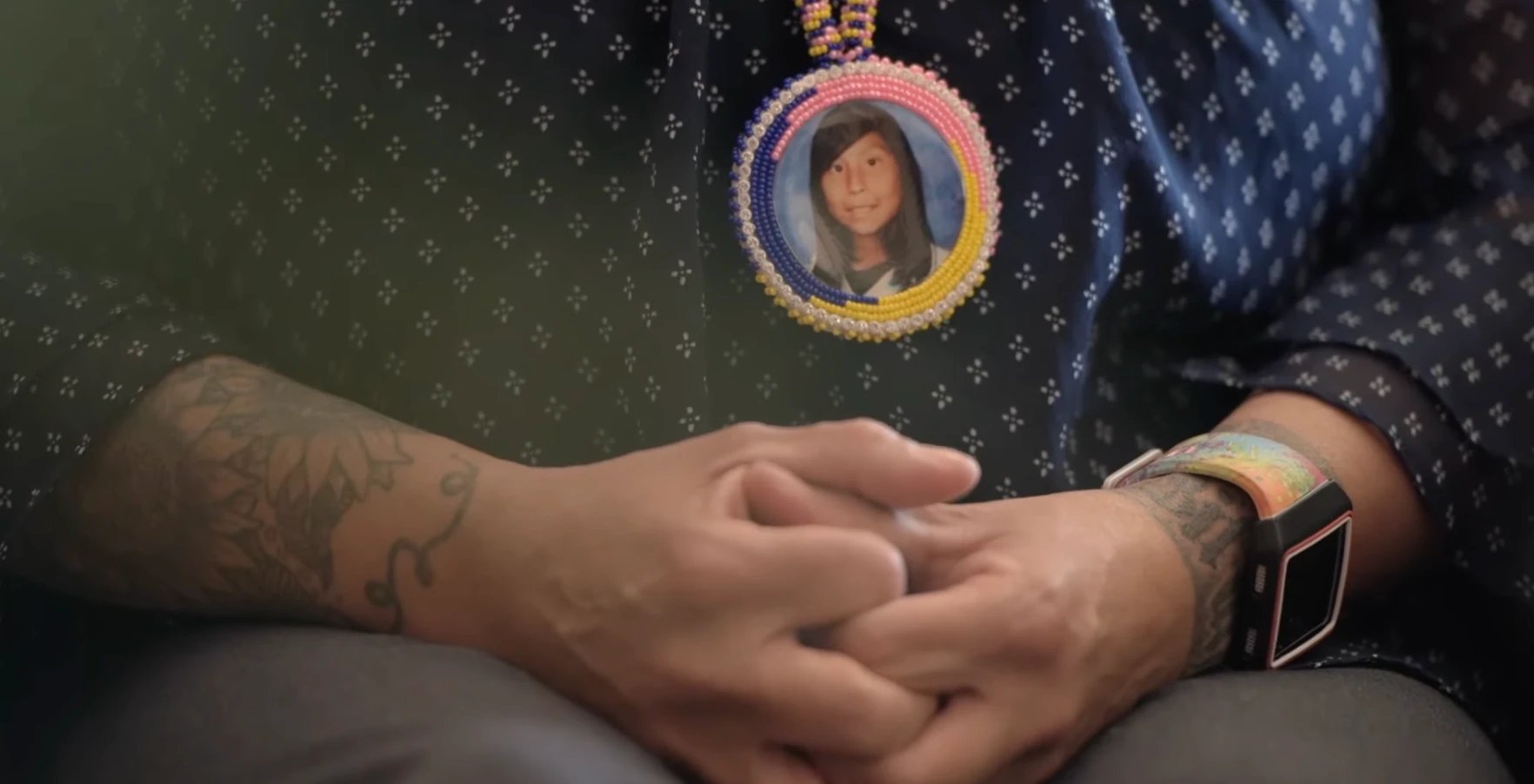 Clasped hands resting beneath a beaded pendant with Ashlynne’s picture.