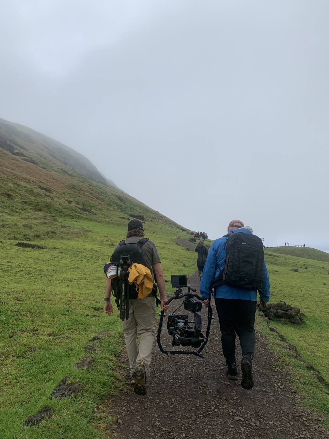 Two crew members carrying a camera rig along a grassy trail at Rano Raraku, Rapa Nui